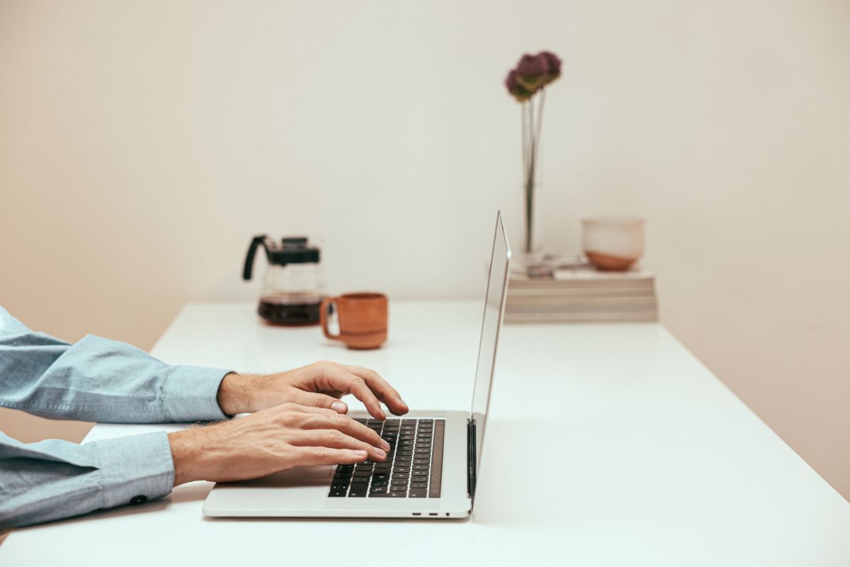 Hands typing on a laptop at a white desk against a soft cream background