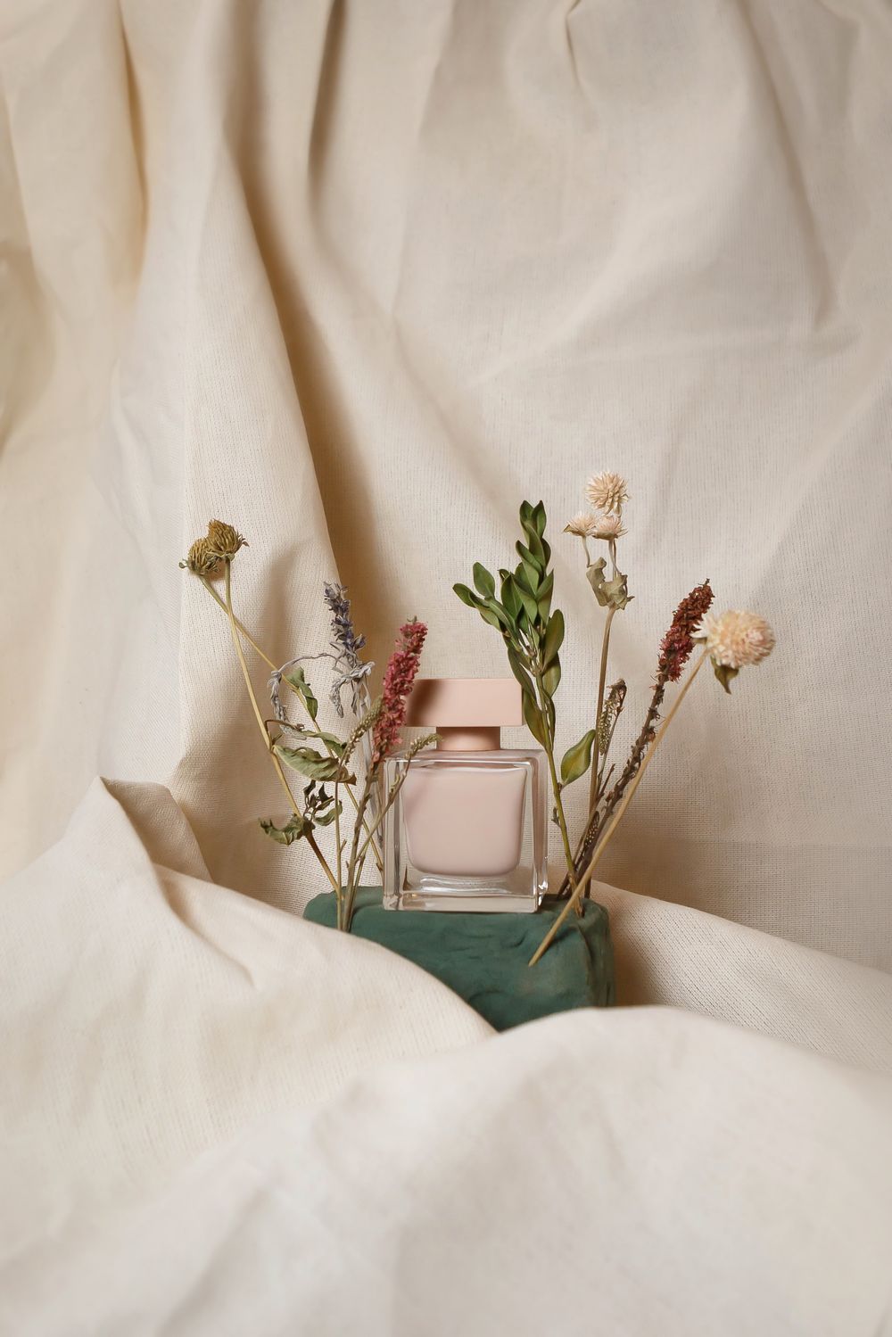 Perfume bottle styled with dried flowers on soft cream fabric