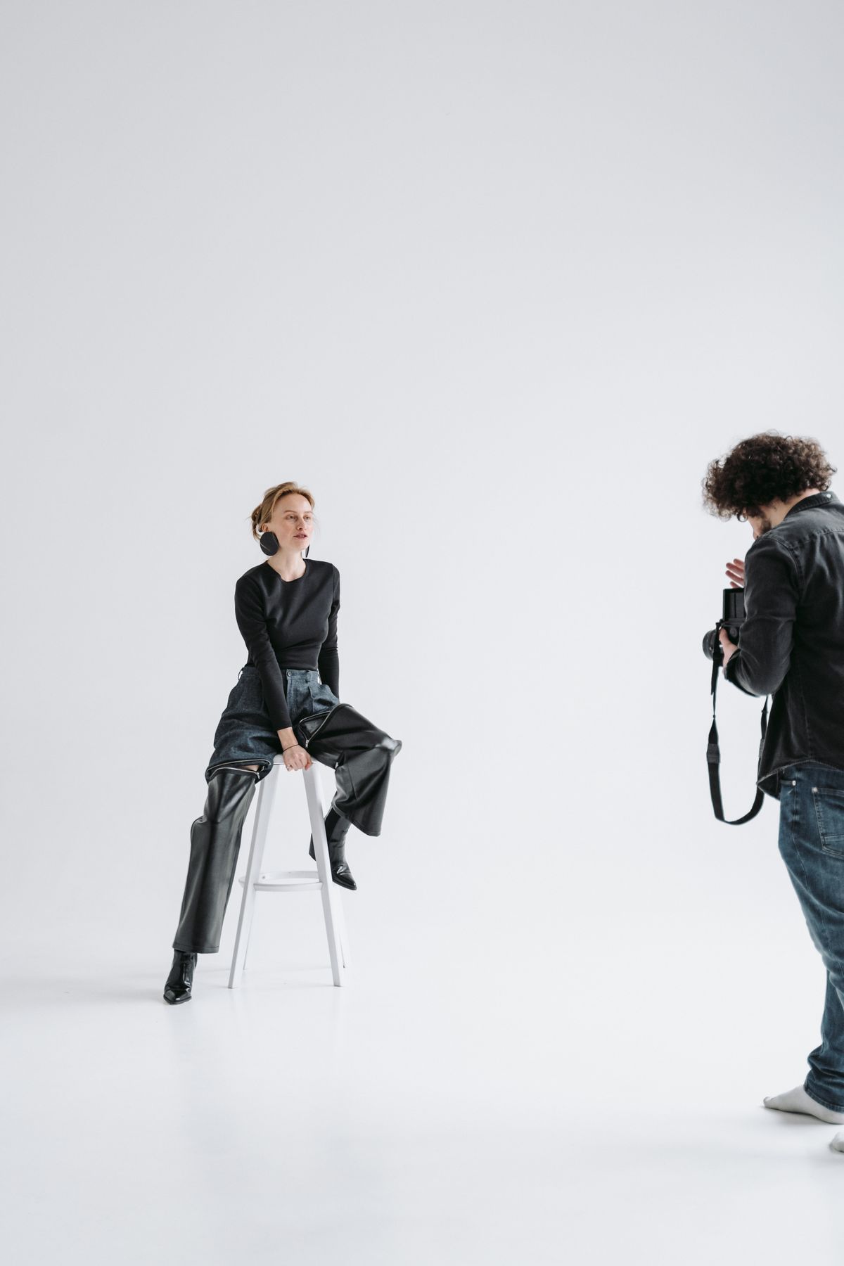 Photographer and seated model during a studio photoshoot against a white backdrop